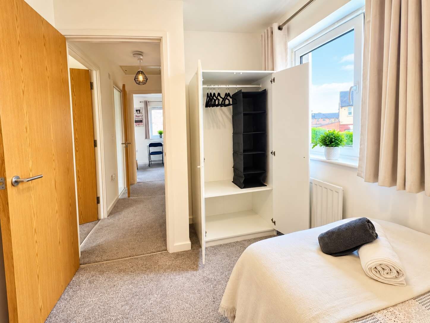 A hotel room with a bed, a wardrobe, a window with curtains, and a view of the outside.