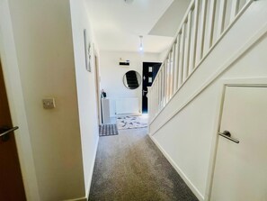 A hallway with a carpeted floor, a white door on the right, and a staircase leading to another room. - 3BR Contractor House Parking 2 Bath (Luton)