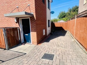 A brick building with a door, a satellite dish, and a paved walkway. - 3BR Contractor House Parking 2 Bath (Luton)