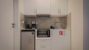 Una cocina compacta con muebles blancos, horno integrado, cafetera y refrigerador.