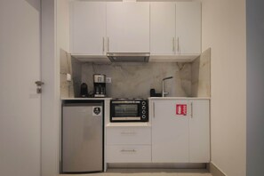 Eine kompakte Küche mit weißen Schränken, einem eingebauten Backofen, einer Kaffeemaschine und einem Kühlschrank.
