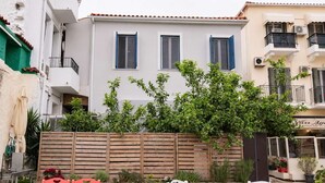 Un edificio con facciata bianca, due finestre con persiane blu e un recinto in legno con vegetazione.