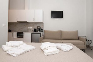 A hotel room with a bed, a sofa, a TV mounted on the wall, a kitchenette, and a small refrigerator. - Limani Blue, Escape Gytheio Hideaway by the Sea (Gytheio)