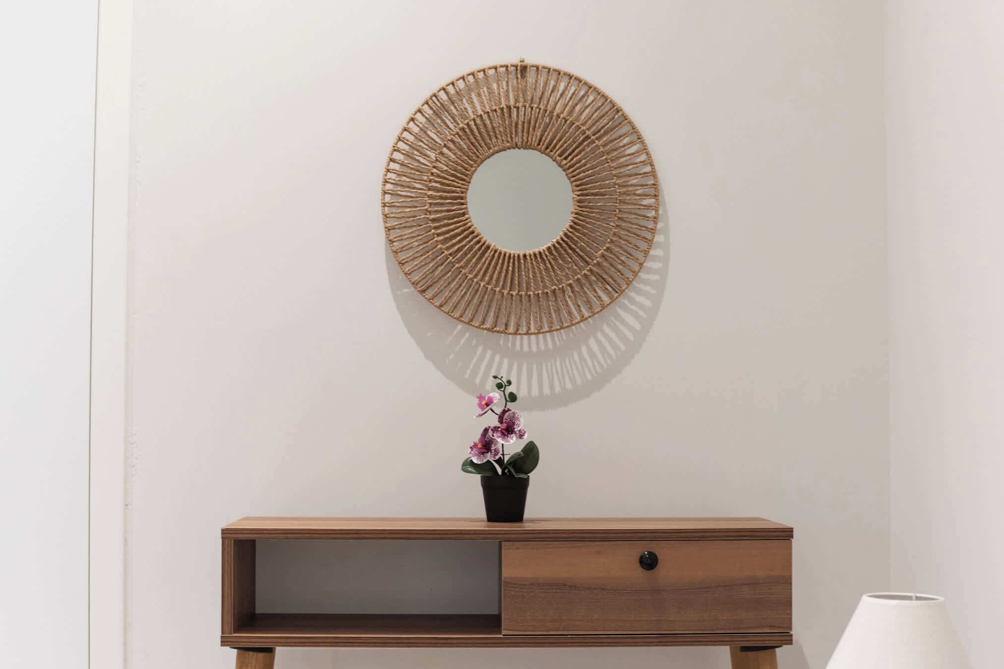 A wall-mounted circular mirror, a wooden cabinet with a drawer, and a potted orchid.