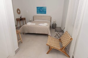 Ein Schlafzimmer mit einem Bett, Nachttischen, einem Stuhl, einem Handtuchhalter und einem Bild an der Wand.