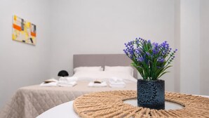 Ein Schlafzimmer mit einem Bett, einem Nachttisch mit Blumenvase und einer Wand mit einem abstrakten Kunstwerk.