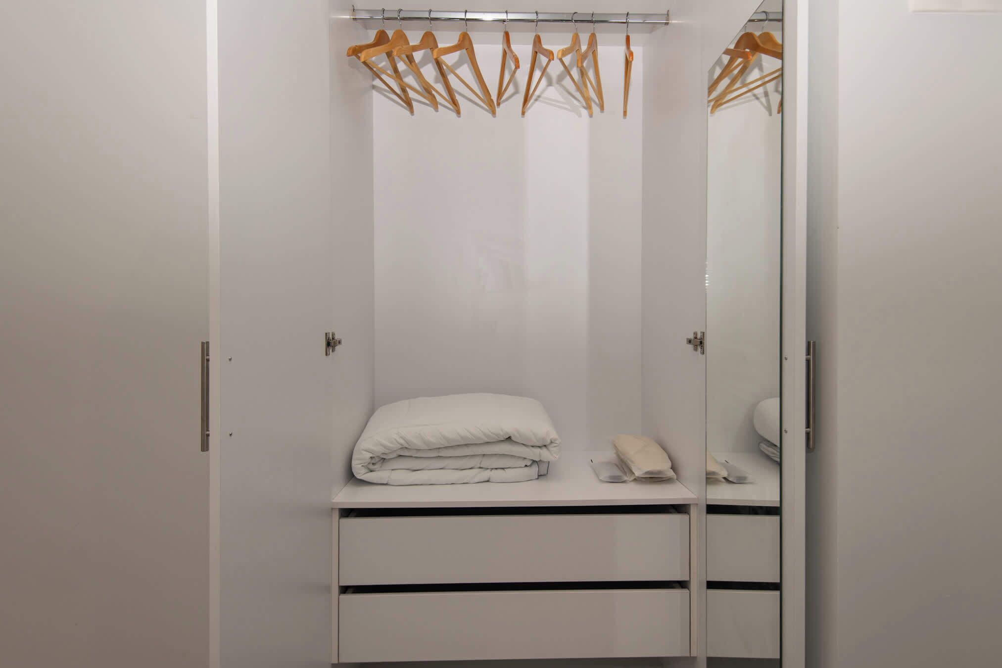 Ein weißer Kleiderschrank mit Spiegel, eine gefaltete weiße Decke und ein kleines Handtuch auf der Ablagefläche.