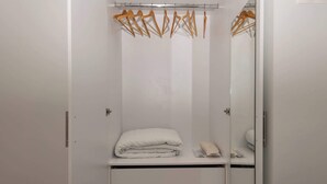 Ein weißer Kleiderschrank mit Spiegel, eine gefaltete weiße Decke und ein kleines Handtuch auf der Ablagefläche.