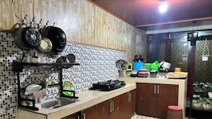 A kitchen with a tiled backsplash, wooden cabinets, a sink, and various kitchen utensils and appliances. - Villa Garcinia 111 Ciwidey (Pasirjambu)