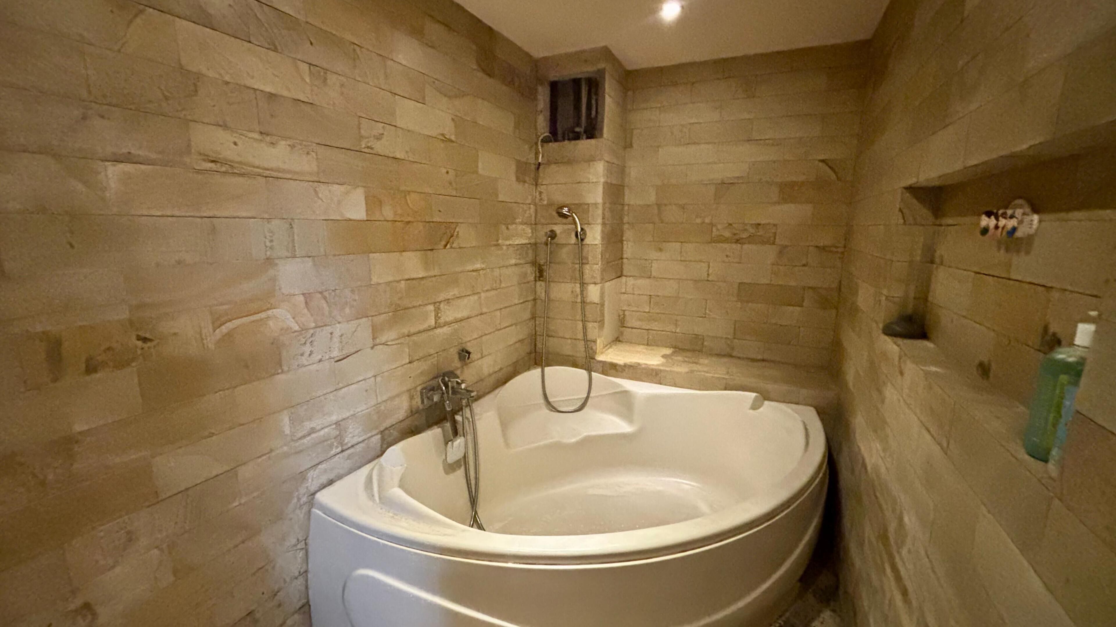 A bathroom with a freestanding bathtub, stone walls, and a shower area.