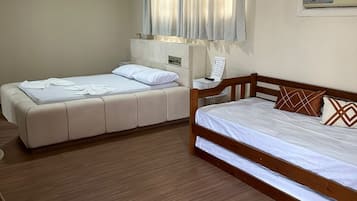 A bedroom with two beds, a wooden floor, a ceiling light, and a window with curtains.