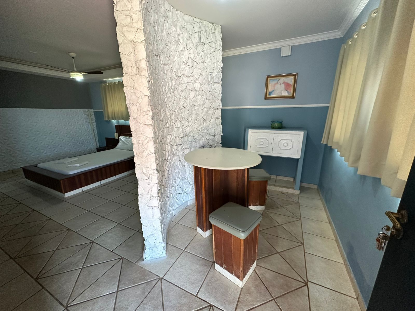 A bedroom with a bed, a small round table, a white cabinet, and a stone accent wall.