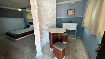 A bedroom with a bed, a small round table, a white cabinet, and a stone accent wall.