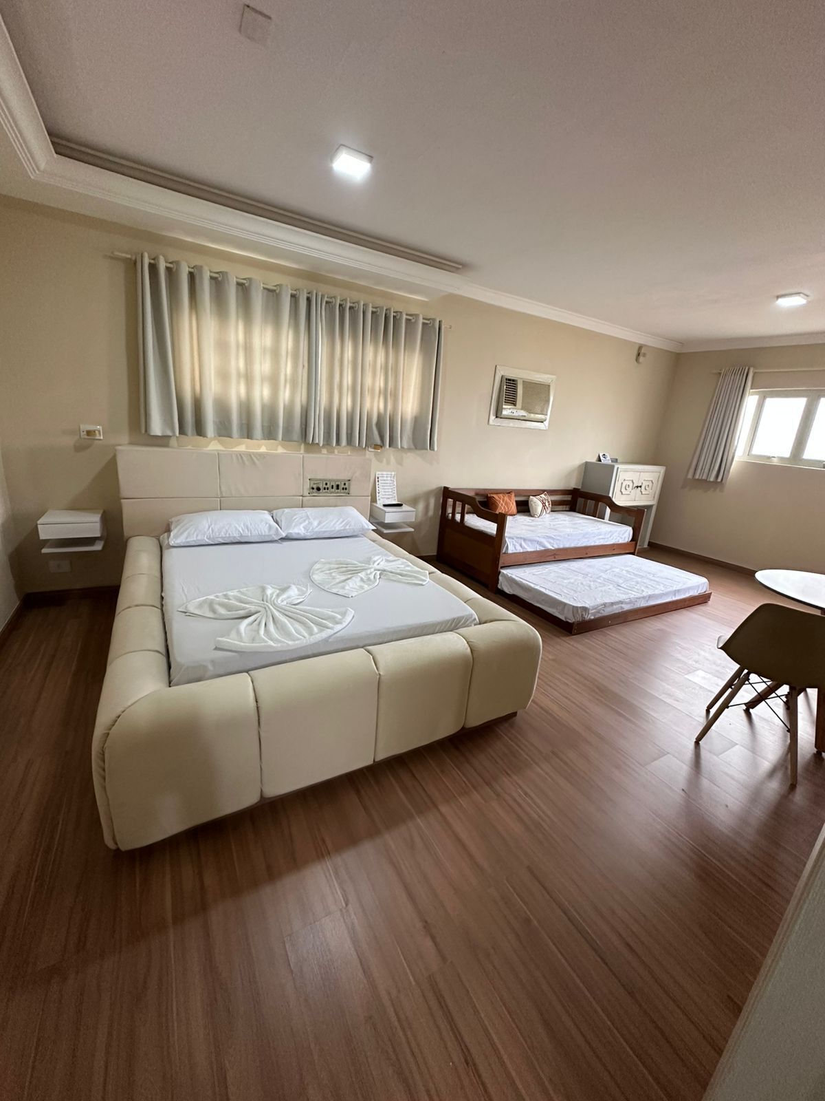 A bedroom with a large bed, a smaller bed, a desk, a chair, and a window with curtains.