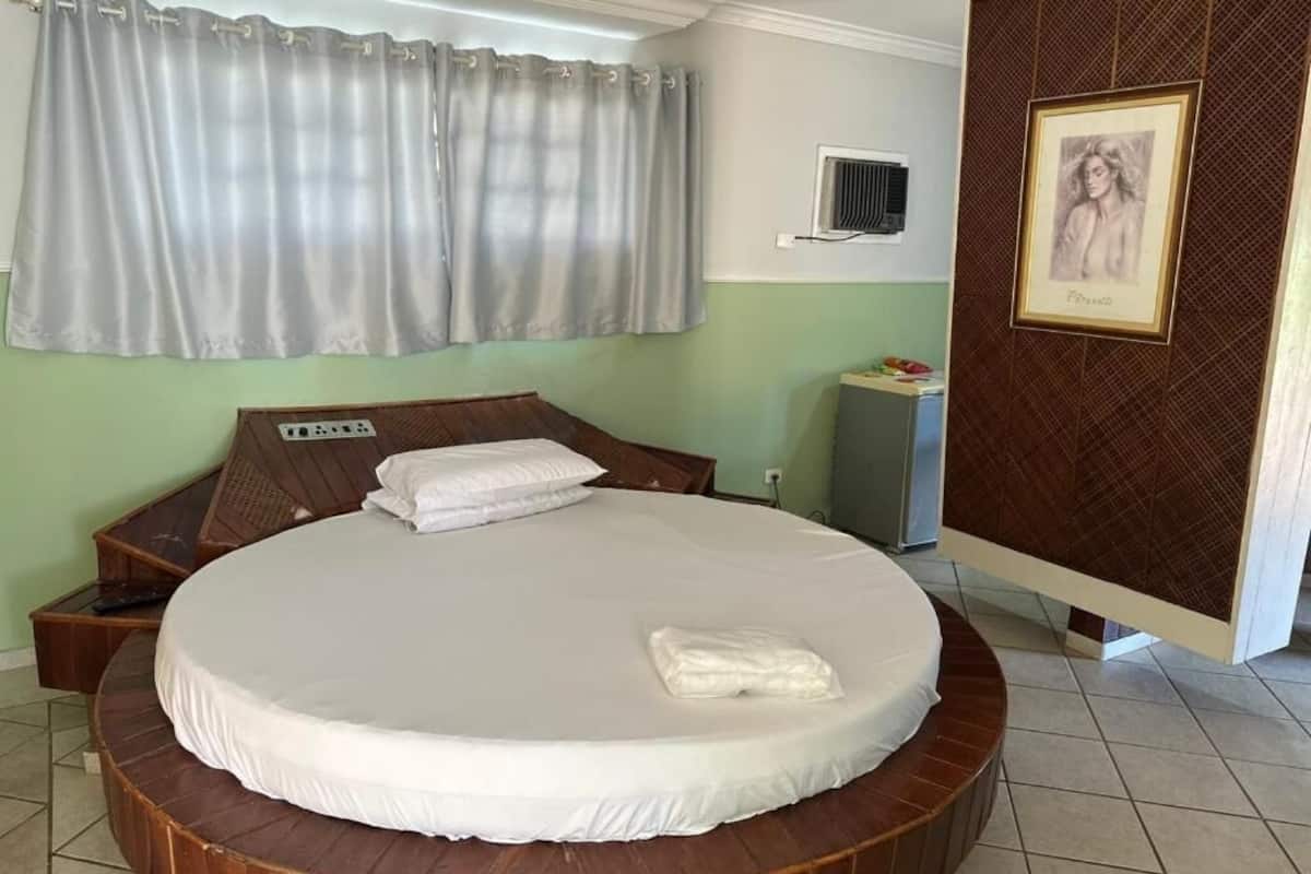 Una cama redonda con colchón blanco, cabecera de madera, mesita de noche y aire acondicionado de pared.