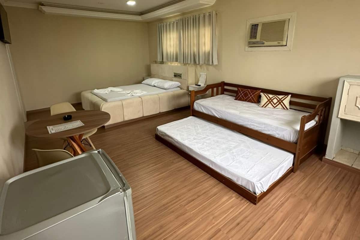 Habitación de hotel con dos camas, un escritorio, una silla, una mesita y un refrigerador.