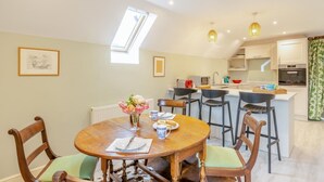 Un coin repas avec une table en bois, des chaises, un vase de fleurs et une cuisine en arrière-plan.
