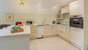 Une cuisine moderne avec des meubles blancs, un lave-vaisselle, un four à micro-ondes et une valise rouge posée sur le plan de travail.