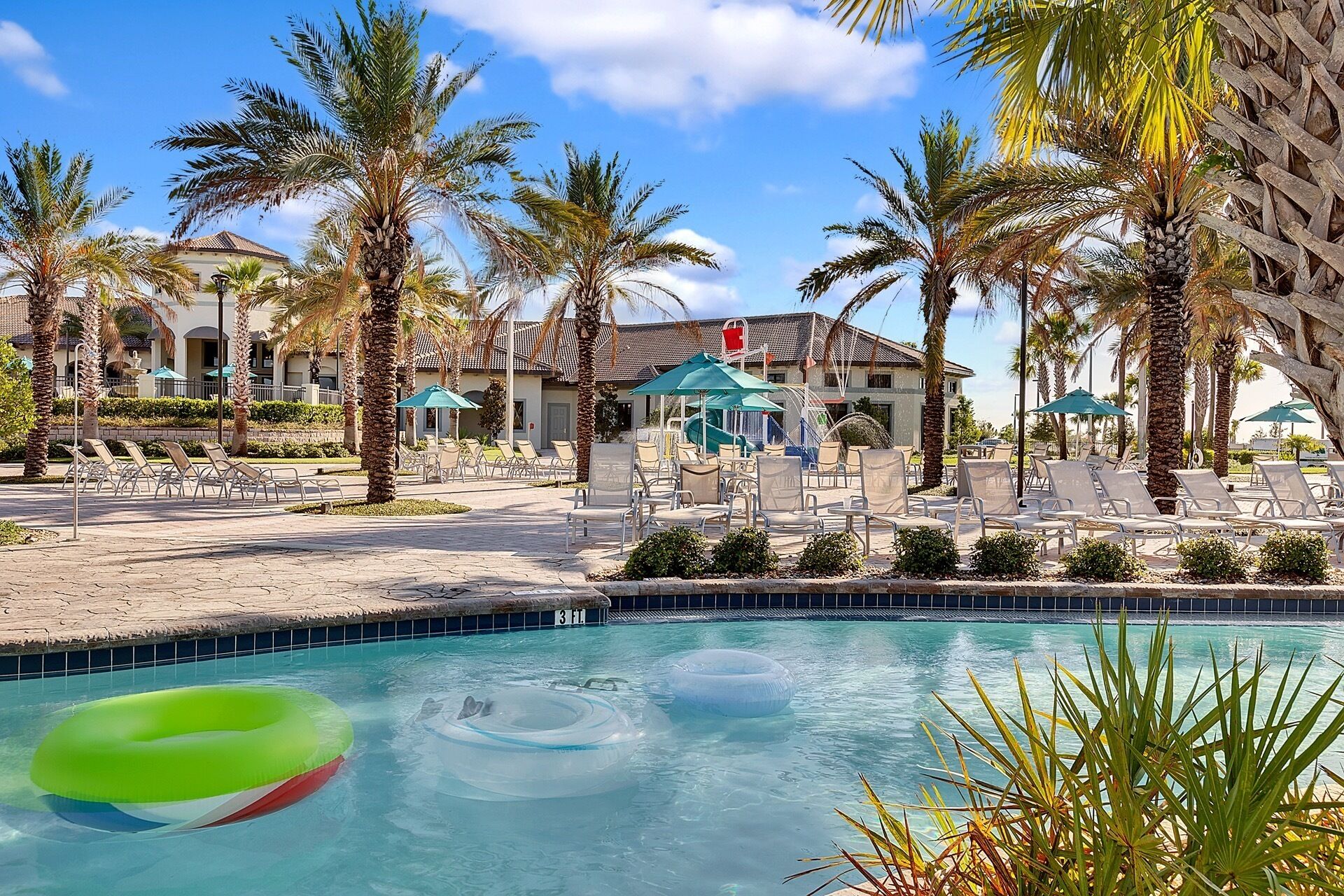 A pool area with lounge chairs, palm trees, and a building with a tiled roof.