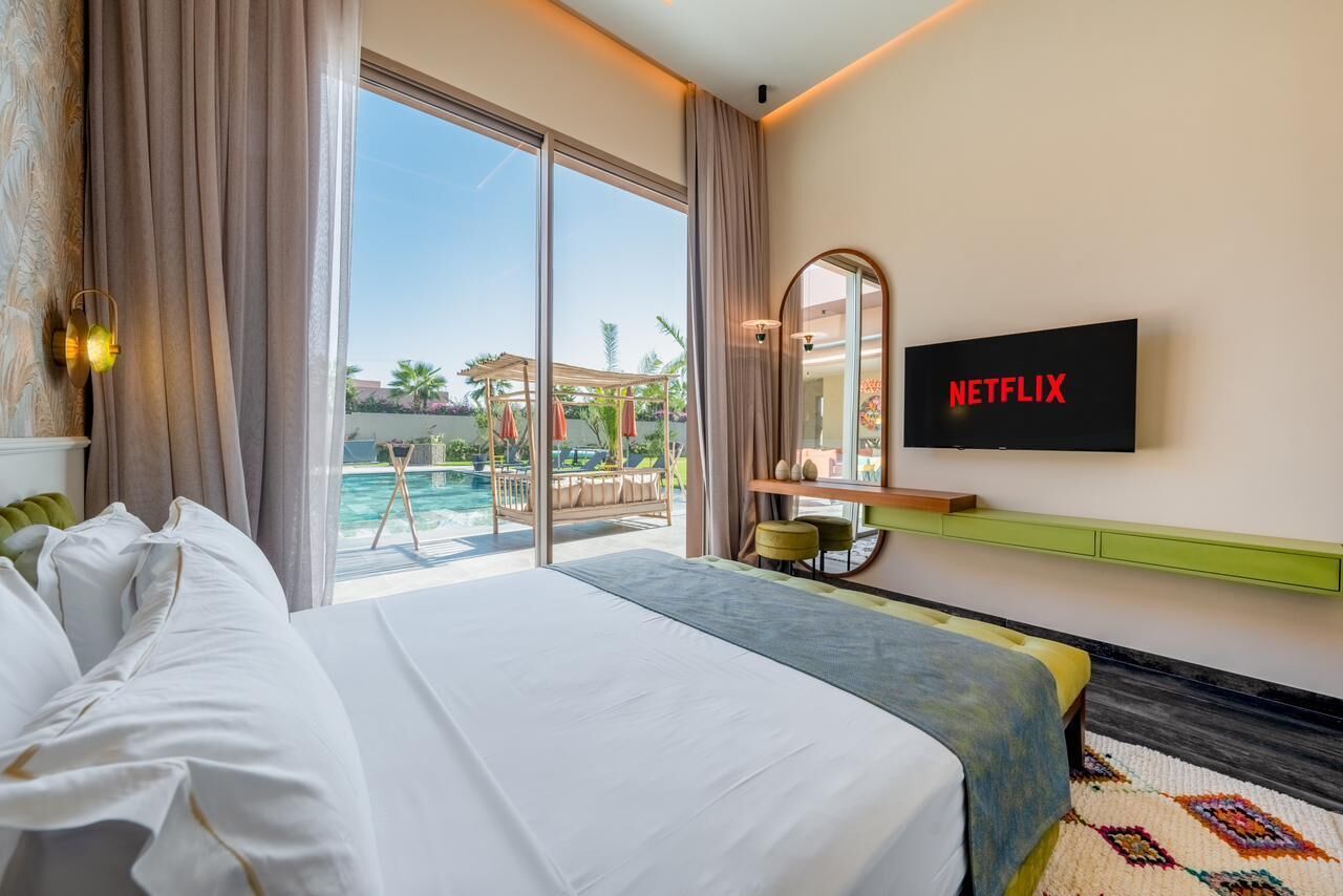 A hotel room with a bed, a TV, a view of an outdoor pool, and a balcony.