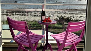 Un balcón con dos sillas rosadas, una mesita con una botella y vasos, y vista a la playa.