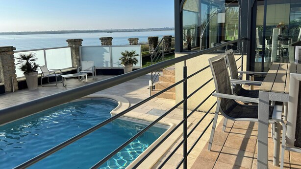 Un balcón con piscina, mobiliario de exterior y vista al mar.