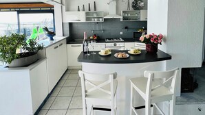 Una cocina moderna con armarios blancos, una isla central con asientos y vistas a un tobogán verde en el exterior.