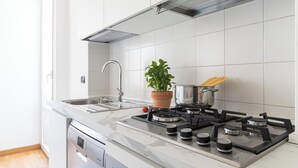 Une cuisine moderne avec un évier en acier inoxydable, une cuisinière à gaz, une plante en pot et une casserole de pâtes.
