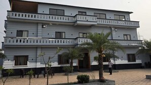 A multi-story building with balconies, a covered entrance, and a paved courtyard with palm trees. - THE FORESTAA RESORT (Haridwar)