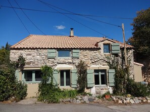 Ein Haus aus Stein mit Ziegeldach, grünen Fensterläden und einem Schornstein.