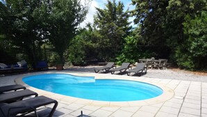 A swimming pool with lounge chairs, a glass table with a plant, and a wooden deck. - Holiday Home 'Bergerie L'Occitane' with Private Pool, Terrace and Wi-Fi (La Caunette)