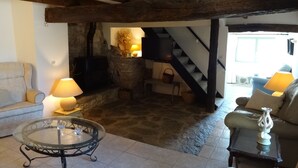 A cozy living room with a stone fireplace, wooden beams, a sofa, a glass table, and a staircase. - Holiday Home 'Bergerie L'Occitane' with Private Pool, Terrace and Wi-Fi (La Caunette)