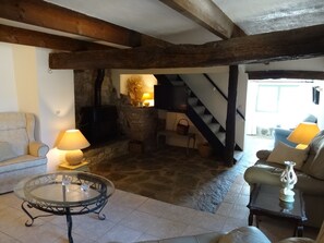 Ein gemütliches Wohnzimmer mit Kamin aus Stein, Holzbalken, einer Couch, einem Glastisch und einer Treppe.
