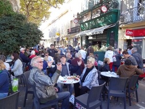 Ein Straßencafé mit runden Tischen und Stühlen, umgeben von Menschen.