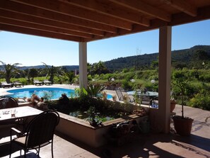 Ein überdachter Außenbereich mit Pool, Liegestühlen und einem Tisch mit Stühlen.