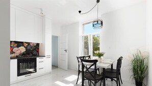 A modern kitchen with white cabinets, a black oven, and a dining area with a white table and black chairs. - Glow - A Cozy Studio in a Great Location (Sopot)