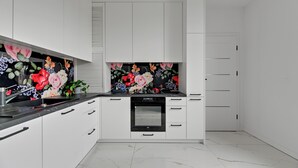 A modern kitchen with white cabinets, a black countertop, and a floral backsplash. - Glow - A Cozy Studio in a Great Location (Sopot)