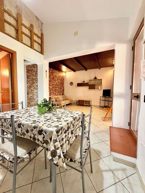 Uma sala de jantar com uma mesa redonda, cadeiras, um vaso de planta e uma parede de pedra.