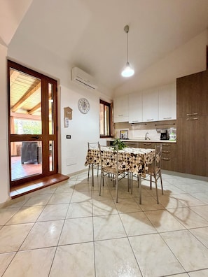 Una cucina spaziosa con zona pranzo, caratterizzata da una porta in legno, pavimento piastrellato e un lampadario.