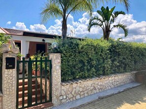 Un muro in pietra, un cancello in metallo e una casa con tetto in tegole.
