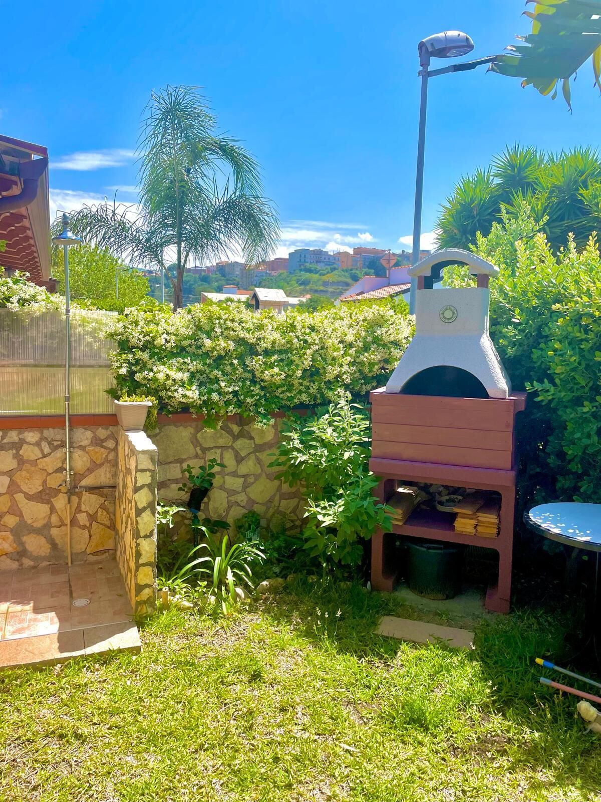 Un jardin avec un barbecue, un mur en pierre et un lampadaire.