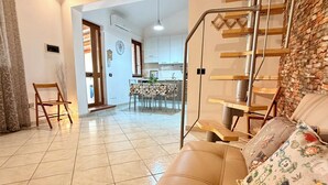 A living room with a sofa, a staircase, and a kitchen in the background. - Steps from the Sea, Minutes from Cefalù (Campofelice di Roccella)