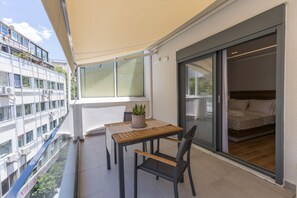 Un balcón con mesa y sillas, una planta en maceta y vista a un edificio de enfrente.