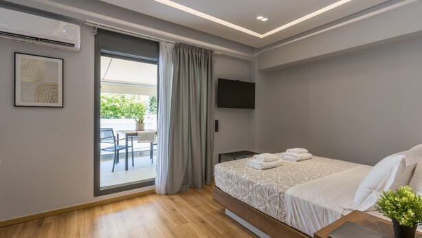 Ein modernes Schlafzimmer mit Bett, Schreibtisch, Laptop, Fernseher und Blick ins Freie.