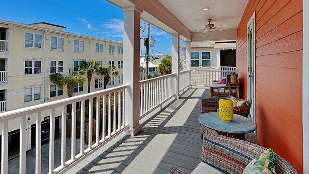 A covered porch with a ceiling fan, a table with chairs, and a view of neighboring buildings. - Chu Cottage (Tybee Island)