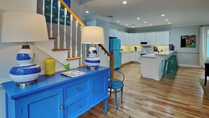 A modern kitchen with wooden flooring, white cabinets, and a blue accent wall. - Chu Cottage (Tybee Island)