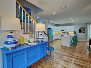 A modern kitchen with wooden flooring, white cabinets, and a blue accent wall. - Chu Cottage (Tybee Island)