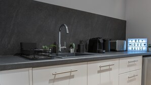 Cozinha moderna com bancada preta, pia de aço inoxidável e armários brancos.