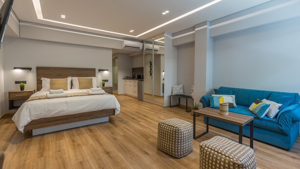 Quarto de hotel moderno com uma cama grande, um sofá, uma mesinha e uma kitchenette.