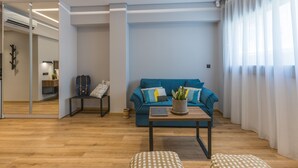 Un salon moderne avec un canapé bleu, une table basse sur laquelle se trouve un ordinateur portable, une plante et un miroir qui reflète la pièce.